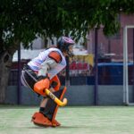 A field hockey goalie in protective gear, ready for action on an outdoor field.