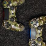 Close-up view of camouflage-patterned game controllers on a dark carpet background.