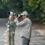 Two wildlife photographers capturing nature scenes with telephoto lenses, standing on a path.