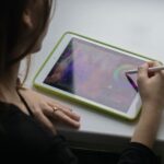 A woman uses a stylus pen on a tablet computer, creating digital art.