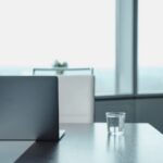 Minimalist office desk featuring a laptop and water glass in a modern business setting.
