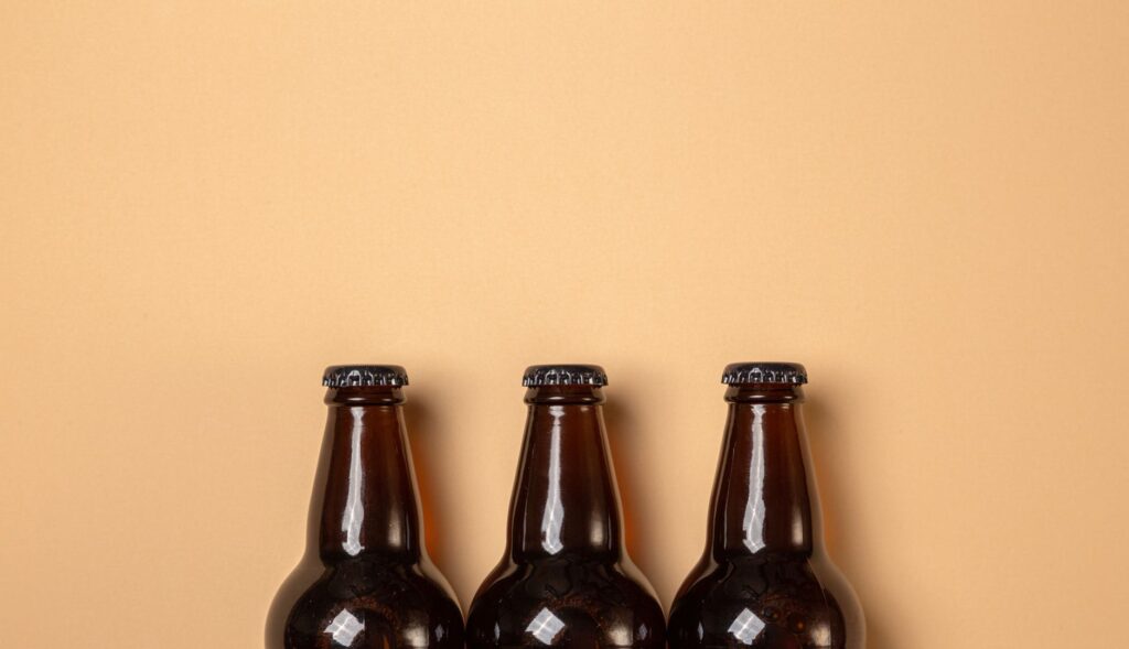 Minimalist still life of three brown beer bottles on a beige background.