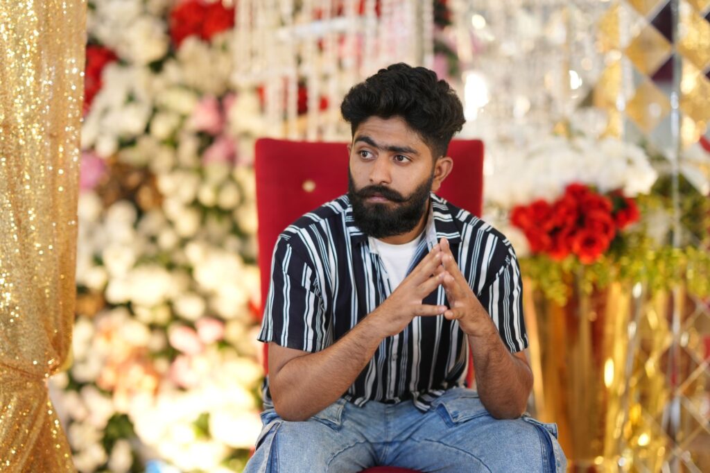A thoughtful man with beard and mustache sitting in a colorful, festive setting.