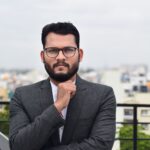 Confident man in business attire standing on an urban rooftop during the day.