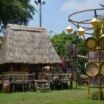 Scenic outdoor view of a traditional thatched-roof hut and cultural art installations under a clear sky.