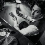 A man counting money with a gun on the desk in a vintage, mafia-themed setting.