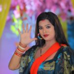 Portrait of a woman in traditional clothing with colorful background, gesturing with hand.