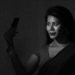 Black and white portrait of an Indian woman in a sari taking a selfie, highlighting grace and technology.