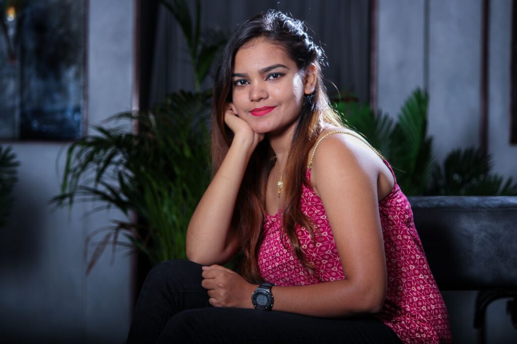 Young woman in a fashionable pose, smiling indoors with lush plants in Chennai.