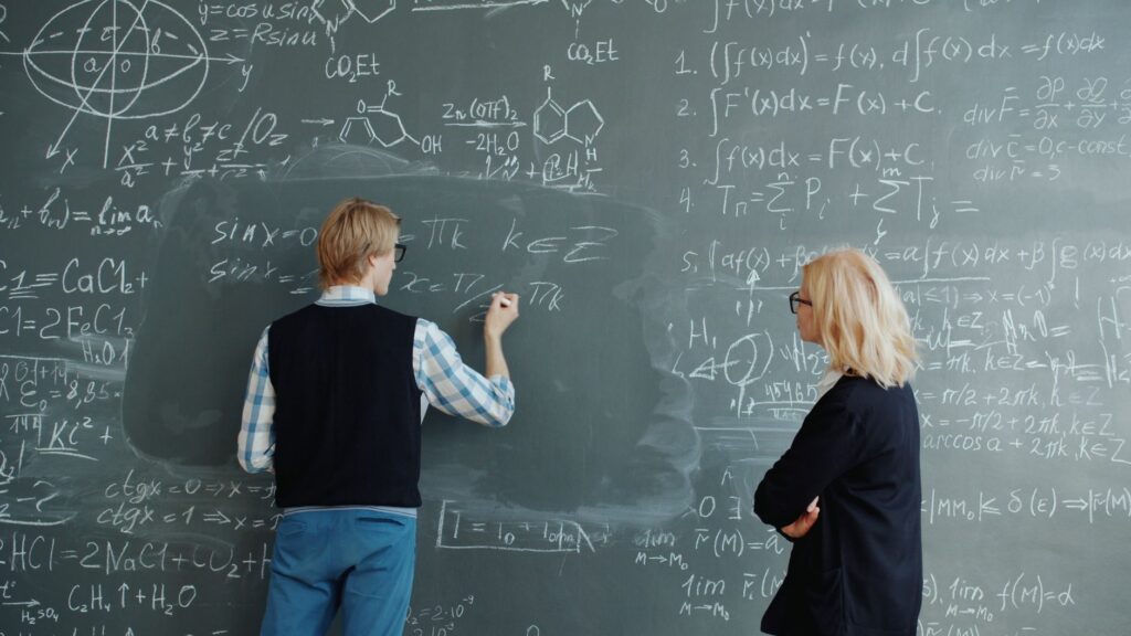 Two professors collaborate on solving complex math equations in classroom.