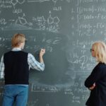 Two professors collaborate on solving complex math equations in classroom.