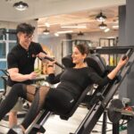 A personal trainer helps a woman with leg presses at a modern gym in Singapore.