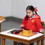 A young girl in a classroom focused on a Montessori educational activity with colorful blocks.