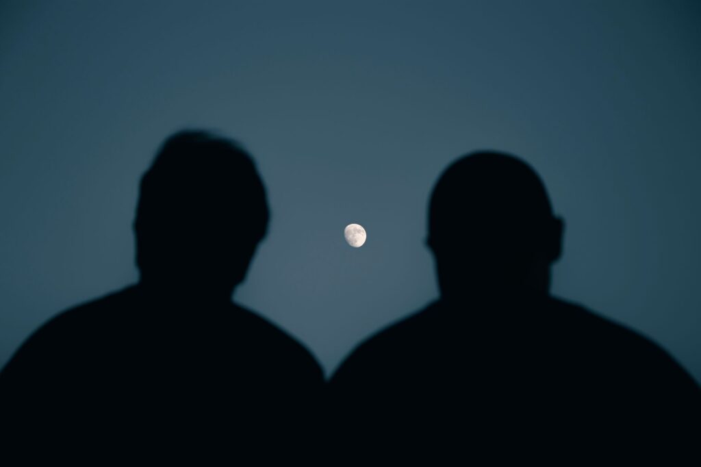 Two silhouettes gaze at the moon in a serene night sky over Mashhad, Iran.