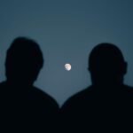 Two silhouettes gaze at the moon in a serene night sky over Mashhad, Iran.
