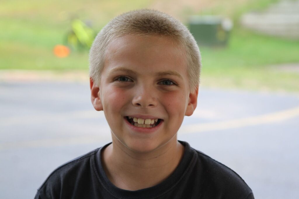 A cheerful young boy with a bright smile in an outdoor summer setting.
