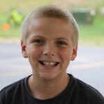 A cheerful young boy with a bright smile in an outdoor summer setting.