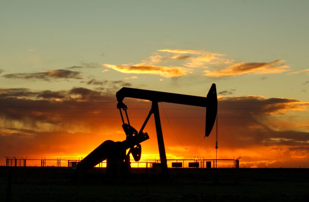 Dramatic silhouette of an oil pump jack against a vibrant sunset sky, emphasizing energy extraction.