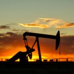 Dramatic silhouette of an oil pump jack against a vibrant sunset sky, emphasizing energy extraction.