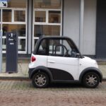 A white and black compact electric car charging at a public power station.