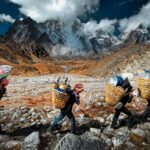 Porters carrying goods through rugged Himalayan terrain in Nepal with dramatic mountain backdrop.
