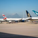 Multiple commercial airplanes parked at an airport terminal with a mountain view in the background.