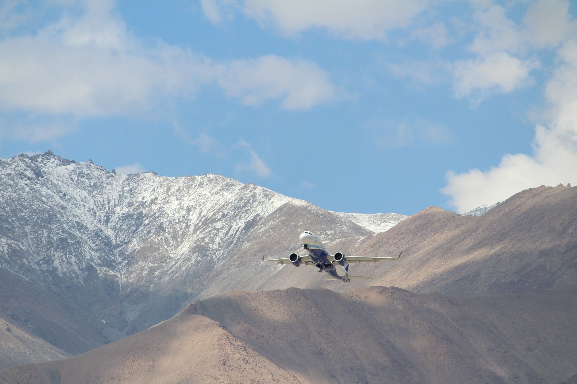 An airplane flies over snow-dusted mountains under a clear blue sky, capturing a sense of adventure and travel.