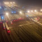 Dramatic aerial night view of a bustling train station with numerous high-speed trains lined up.