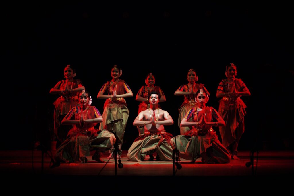 Captivating Indian classical dance performance with traditional costumes and dramatic red lighting on stage.