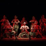 Captivating Indian classical dance performance with traditional costumes and dramatic red lighting on stage.