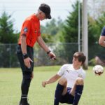 A soccer referee assists an injured player on a sunny outdoor field.