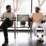 Two adults chatting in a bright barbershop while waiting, showcasing casual interaction.