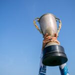 Hands holding a trophy high against a clear blue sky, symbolizing victory and success.