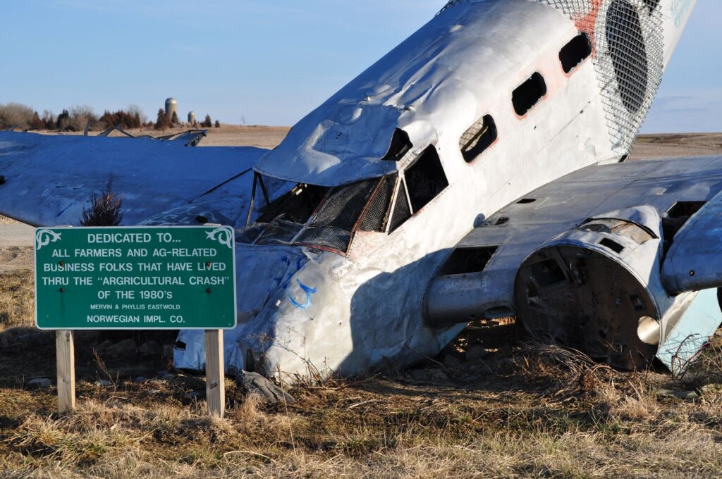 A wrecked airplane amid an open farmland, symbolizing the agricultural crash of the 1980s.