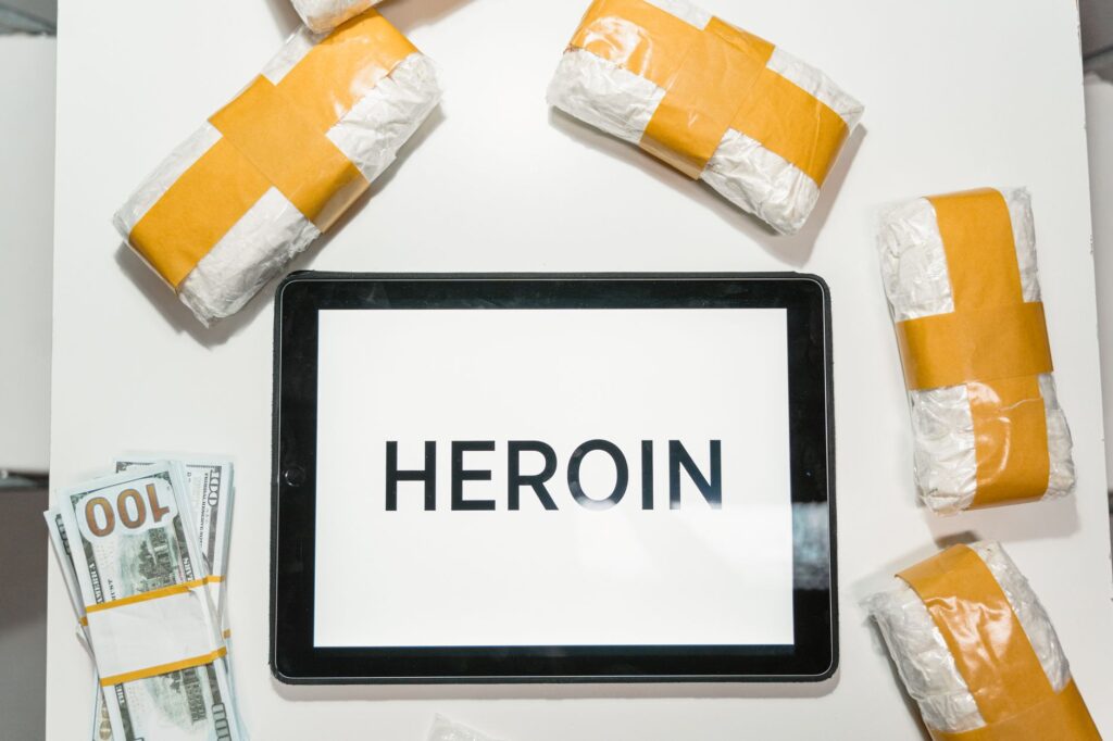 Conceptual image showing packaged heroin, money, and tablet with text in a flat lay arrangement.