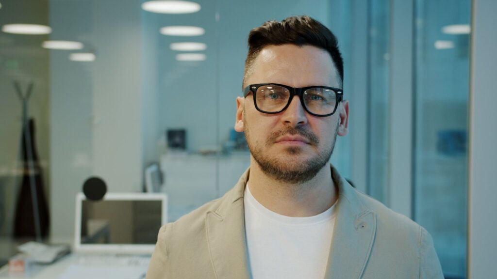 Portrait of a man with glasses in a modern office environment, looking serious.