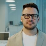 Portrait of a man with glasses in a modern office environment, looking serious.