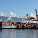 Container ship docked at Vancouver's bustling port with cranes and mountains in view.