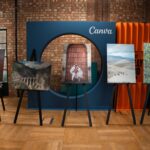 A modern indoor art exhibition showcasing diverse photography on easels against a brick wall.