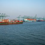 A bustling shipping port featuring container ships and crane operations under clear skies.