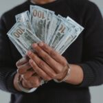 Close-up of hands holding 100-dollar bills while handcuffed, symbolizing crime and punishment.