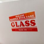 Close-up of a glass packaging label with 'Handle with Care' warning text on a white box.