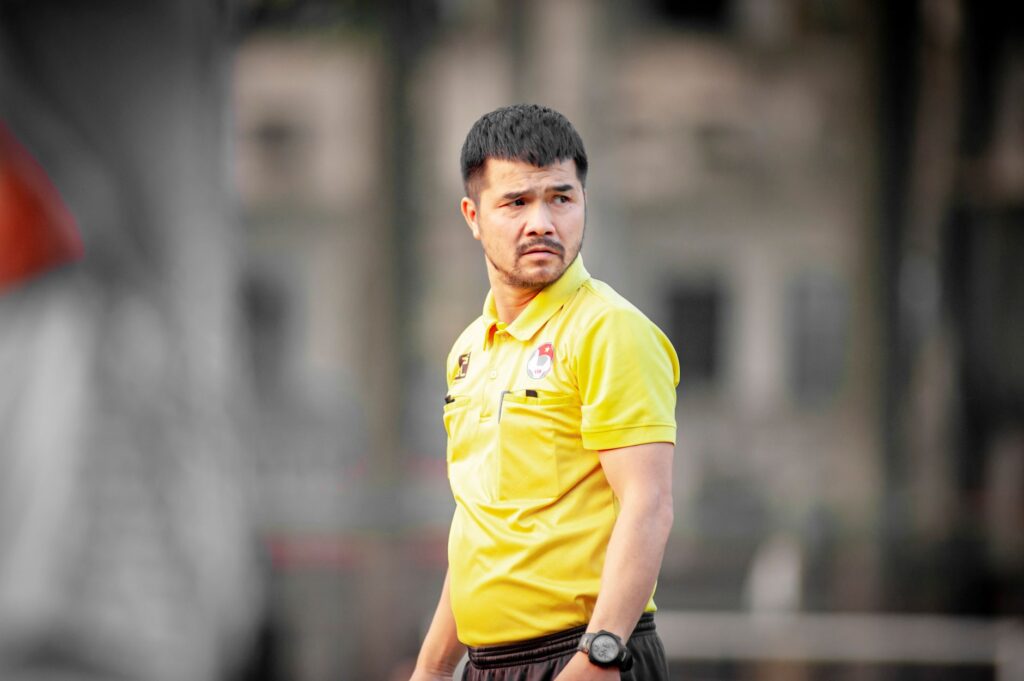 Focused soccer coach wearing yellow shirt during outdoor training session in Hanoi, Vietnam.