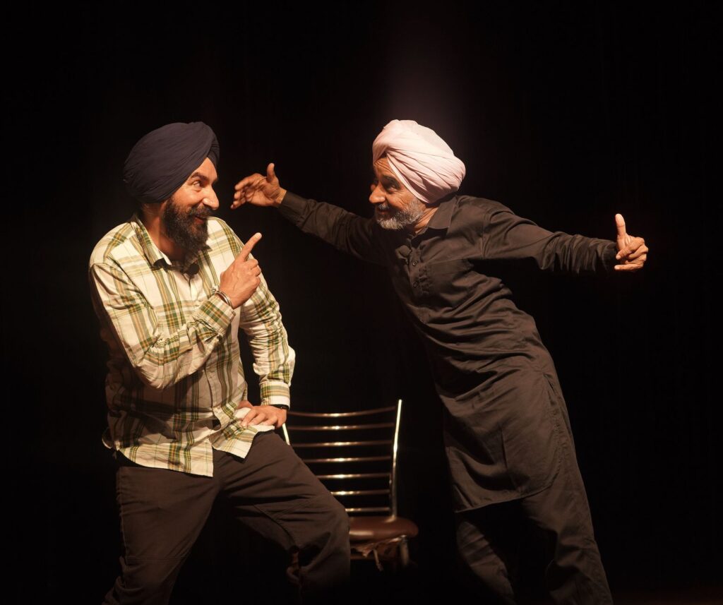 Two men in traditional turbans enjoying a lively performance on stage, expressing joy and interaction.