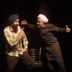 Two men in traditional turbans enjoying a lively performance on stage, expressing joy and interaction.