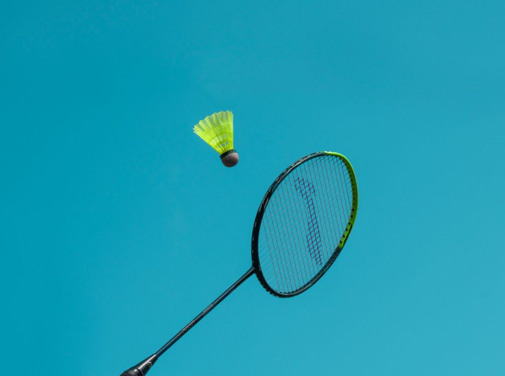 A thrilling action shot of a badminton racket hitting a shuttlecock against a clear blue sky.