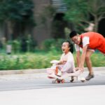 Joyful siblings playing with a toy car in an urban park setting in Jiujiang, China.