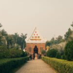 Serene temple entrance nestled in lush gardens under a clear sky, inviting visitors to explore.
