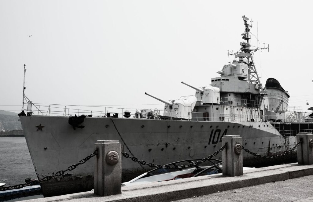 A large naval destroyer ship docked at a harbor under a gray sky.