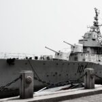 A large naval destroyer ship docked at a harbor under a gray sky.